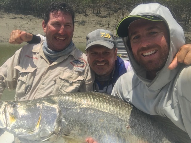 Three anglers laughing together over a barra in the mangroves