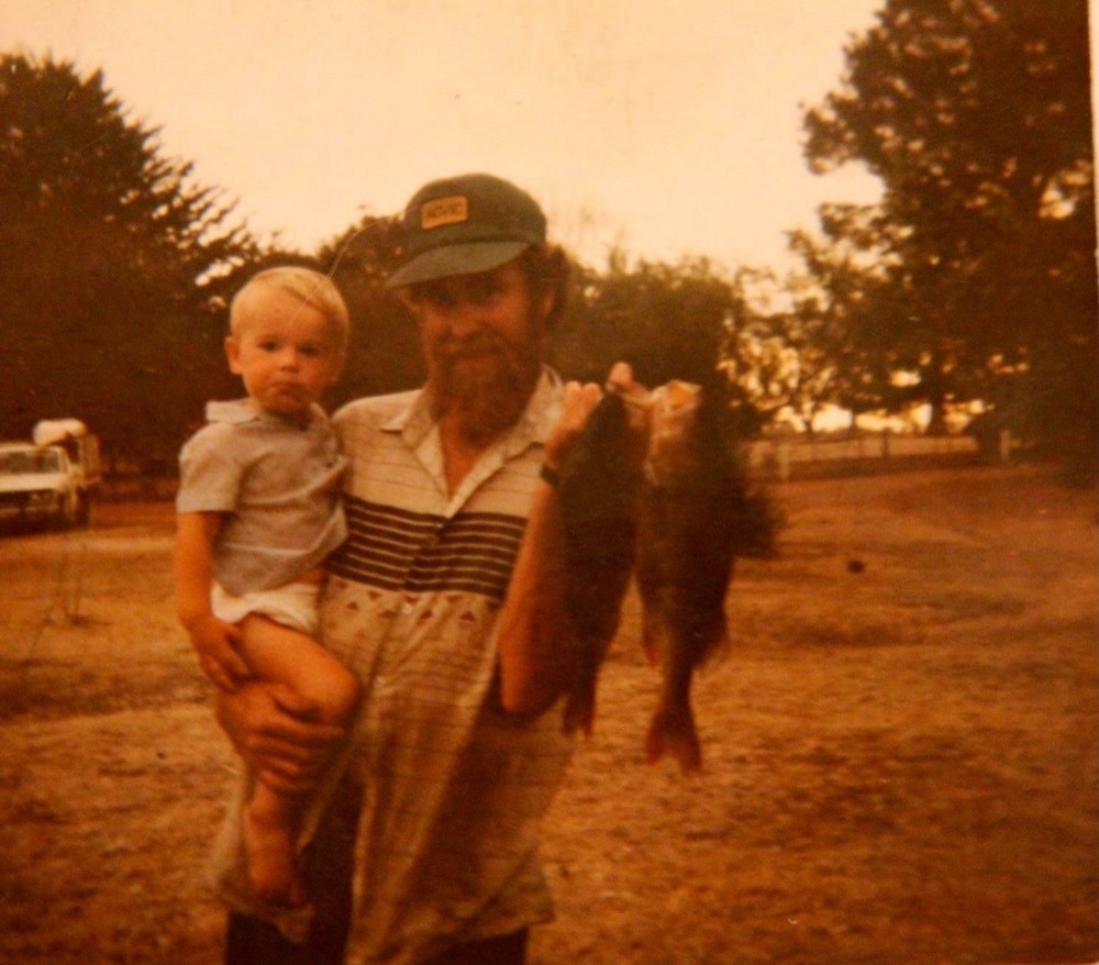 Faded family photo of a bearded dad holding a toddler and a pair of redfin on the farm