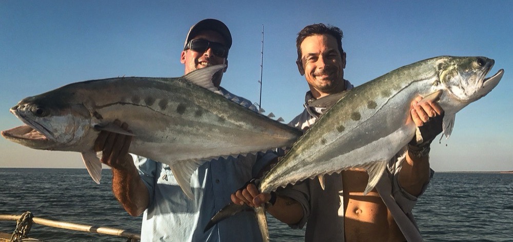 Two anglers holding up a pair of big queenfish in golden evening light