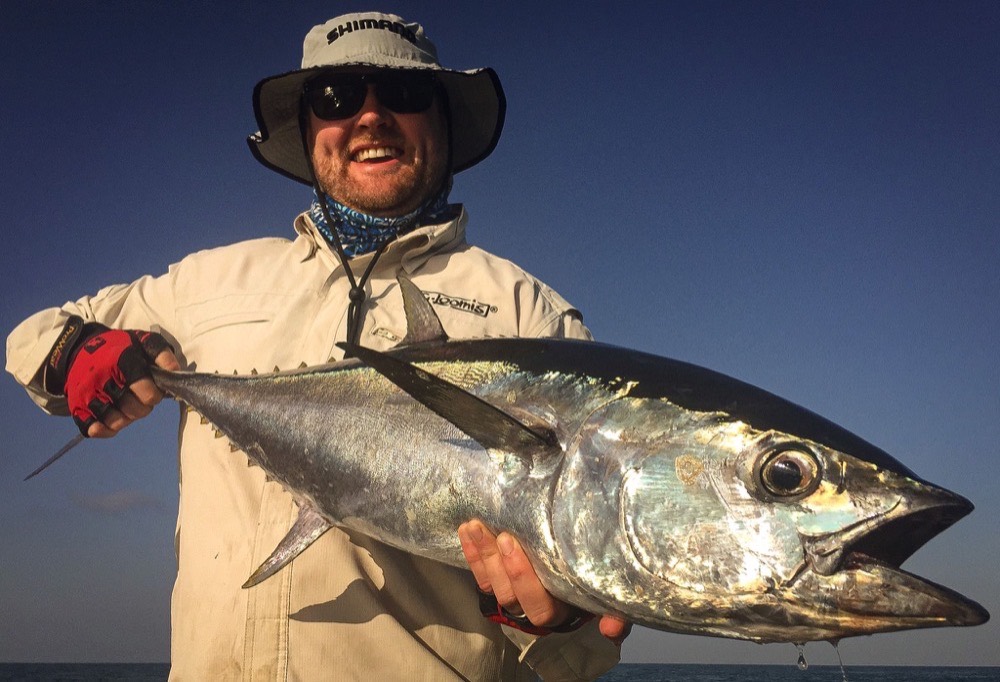 Angler holding a gleaming longtail tuna against a deep blue sky