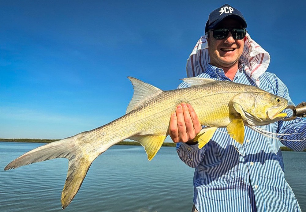 Grinning angler holding a golden king threadfin salmon on calm Bynoe water