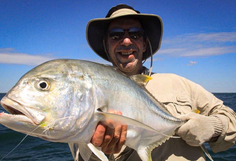 Angler holding a golden trevally on clean dry-season water at Bynoe