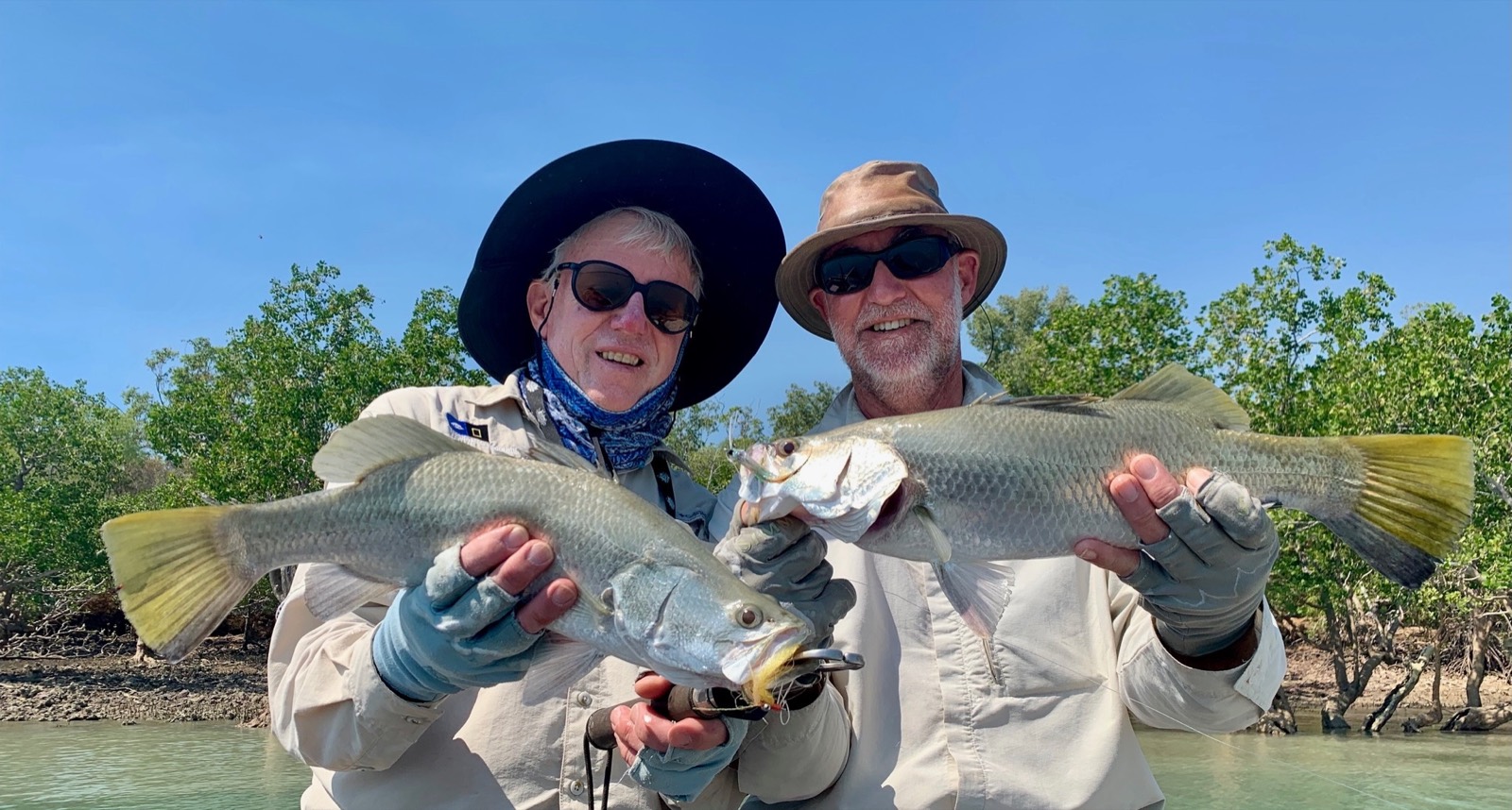 Two fly anglers grinning with a double hook-up of barramundi against the mangroves