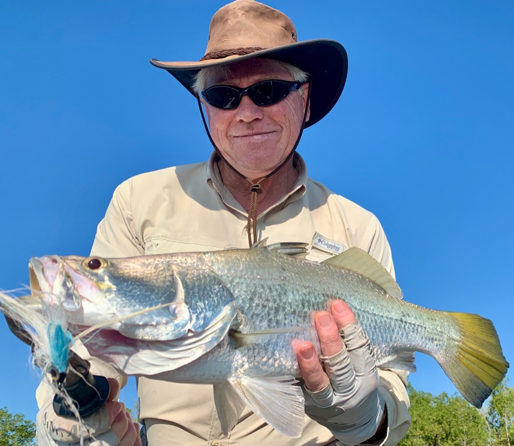Fly angler holding a chrome barramundi with the blue fly still pinned in its jaw