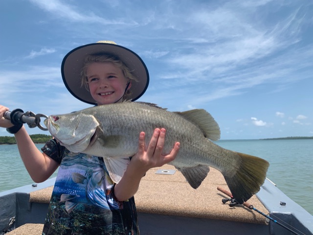A kid waving from the boat with a barra on the deck