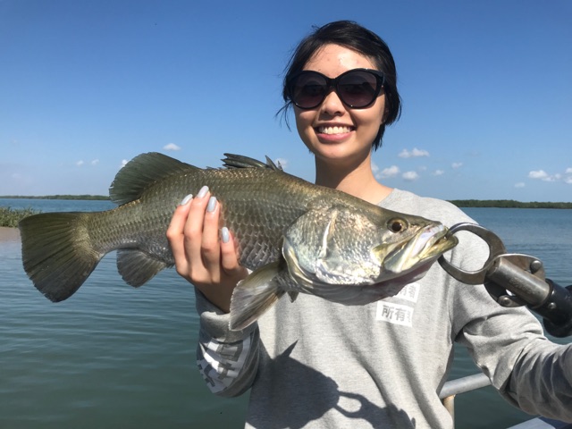 Angler in sunglasses holding a barramundi on the flats