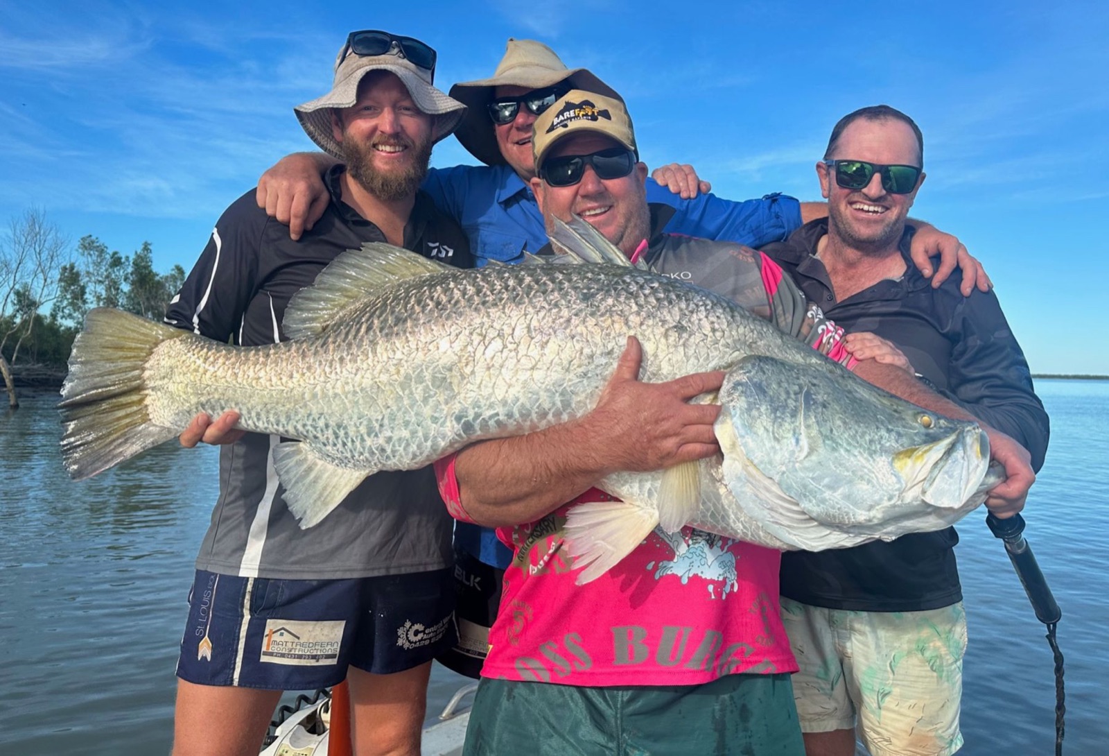 Four happy anglers on a Barefoot boat holding a huge silver barramundi together