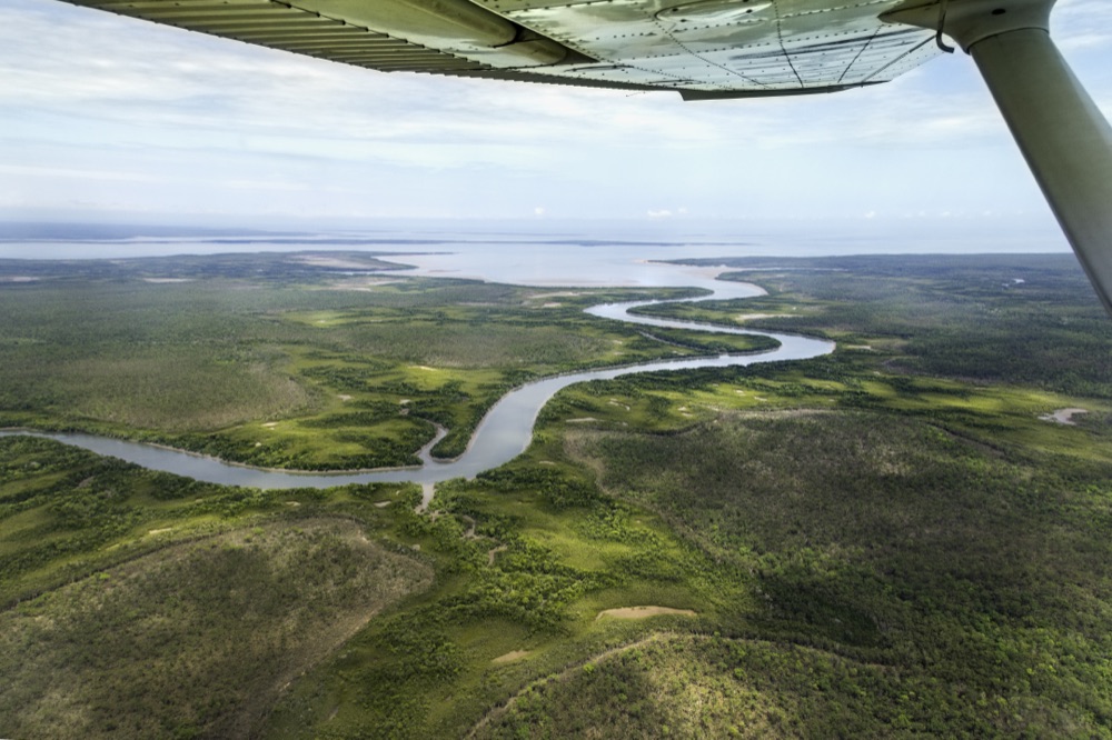 Aerial view from a light plane of a Top End river winding through green floodplain country out towards the coast