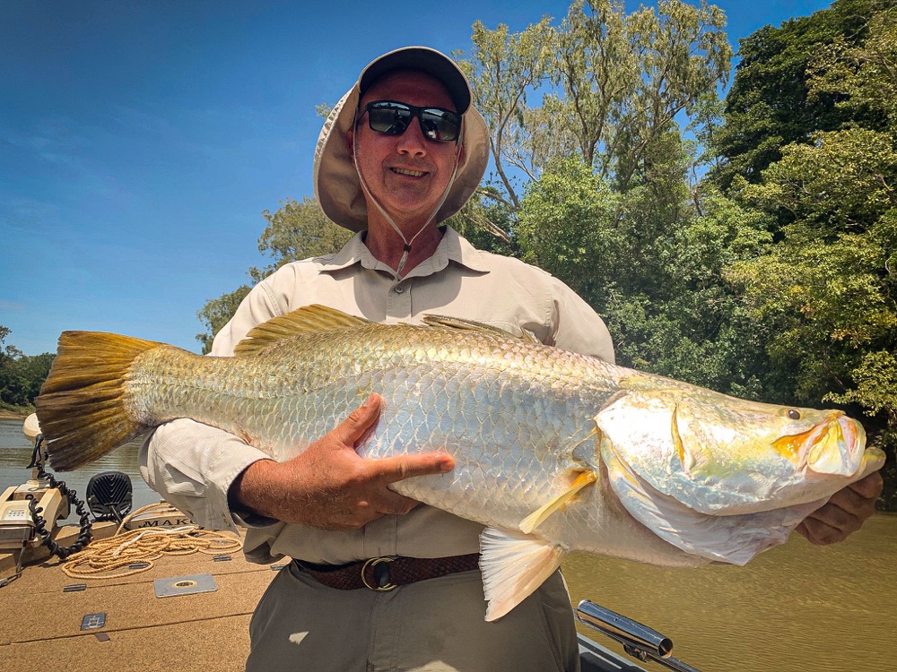 Angler holding a big golden barramundi on a shady run-off river