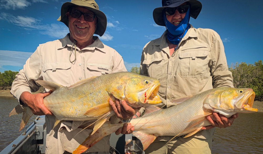 Two anglers each holding a big golden king threadfin salmon under a blue Top End sky