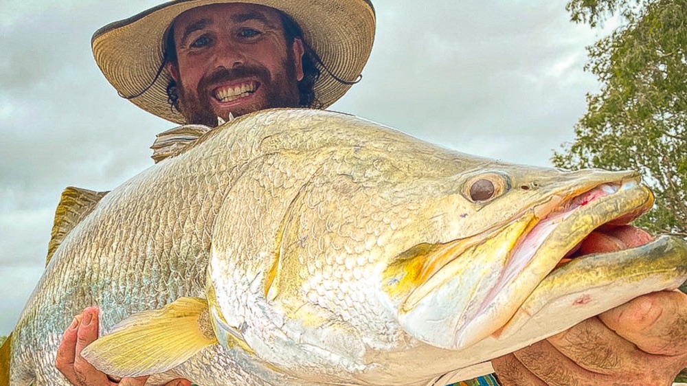 Watty in his straw hat grinning behind a big golden barramundi